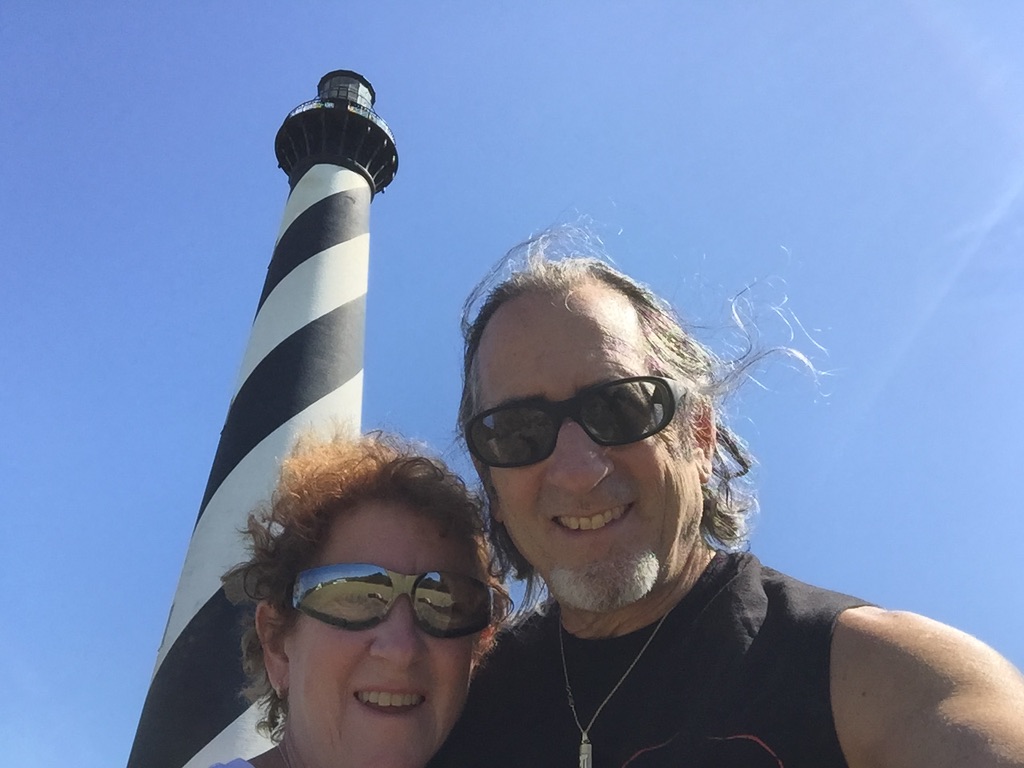 Couple smiling near black-and-white lighthouse.