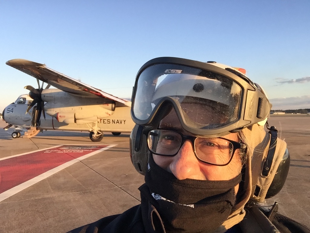 Person in gear near military aircraft on tarmac.