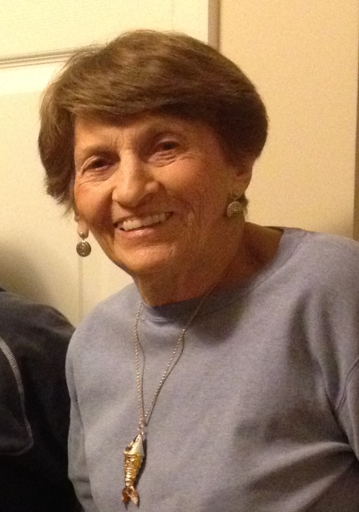 Elderly woman smiling, wearing a necklace.