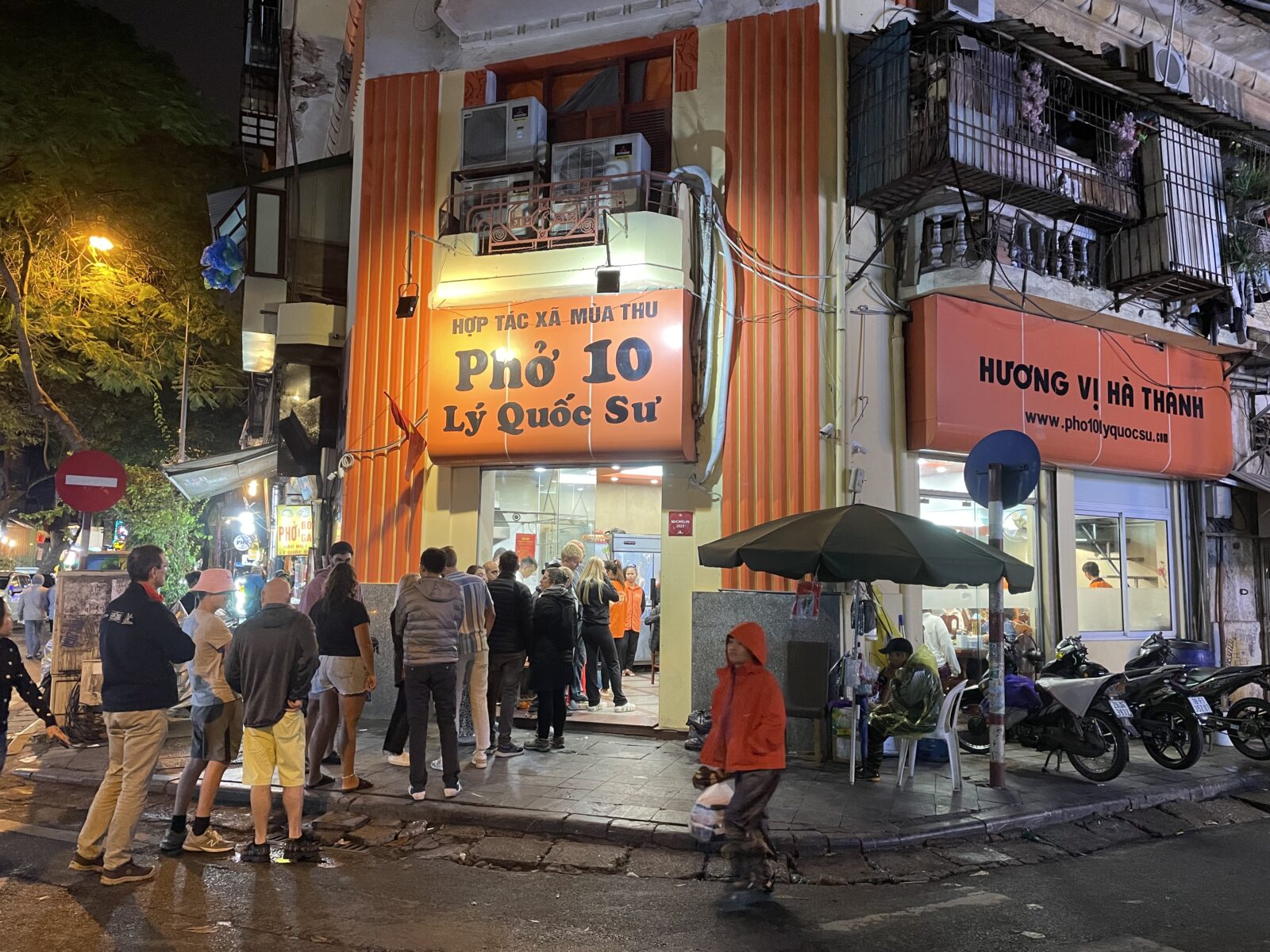 A group of people standing on the sidewalk in front of a building.