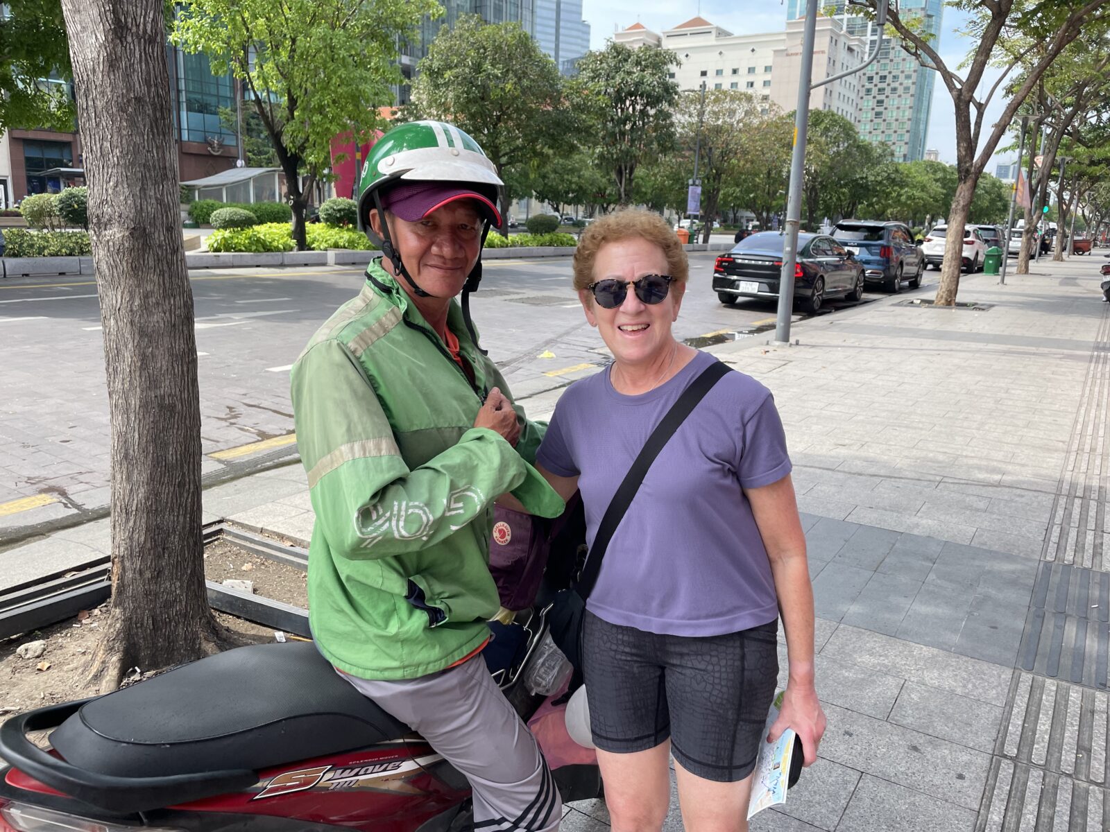 A woman standing next to another person on a motorcycle.